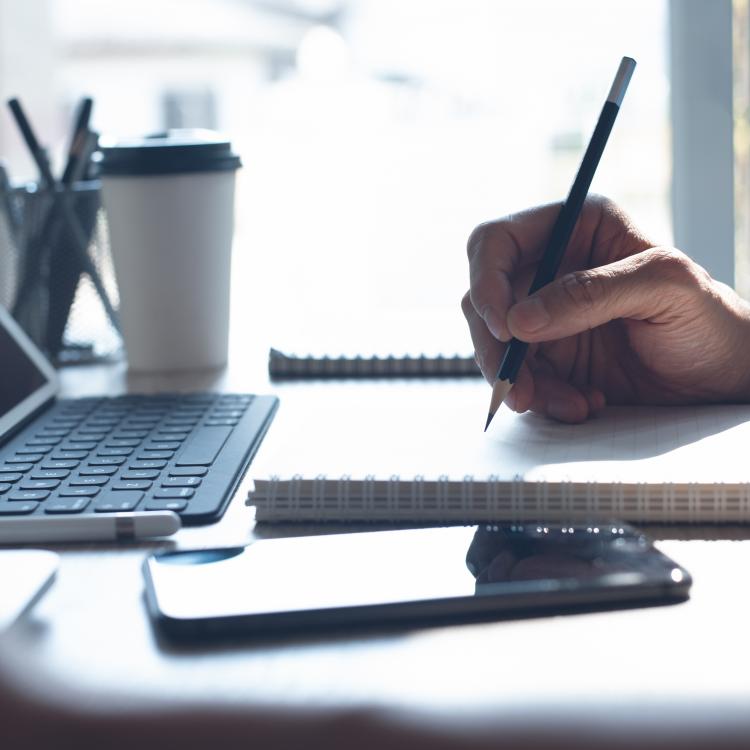  Person writing on notepad in front of laptop